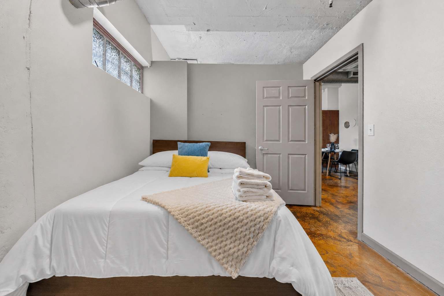 Un dormitorio con cama, almohadas, manta y puerta que da a un comedor.