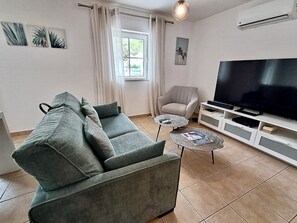A living room with a grey sofa, a chair, a TV, and a small table with magazines. - 1-Bedroom Apartment Near the Beach in Cabanas with a Parking Space (Cabanas de Tavira)