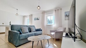 A living room with a sofa, armchair, round table, and a TV stand. - 1-Bedroom Apartment Near the Beach in Cabanas with a Parking Space (Cabanas de Tavira)