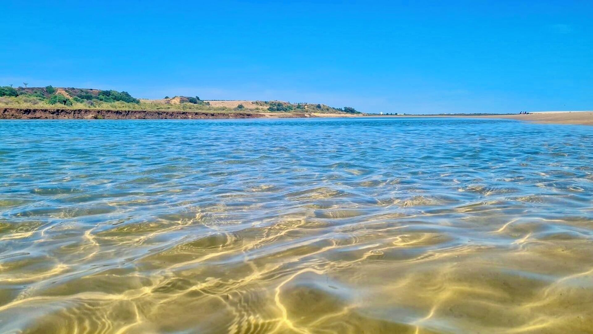 Ein freier Blick auf einen Strand mit ruhigem Wasser und weiter Küste.