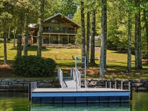A lakeside cabin with a dock, surrounded by trees and a grassy area. - Lakefront Lodge w Dock, Fire Pit & Views! (Cullowhee)