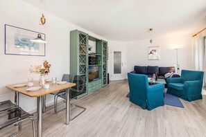 Un salon moderne comprenant un coin repas, des fauteuils turquoise, un téléviseur et une bibliothèque.