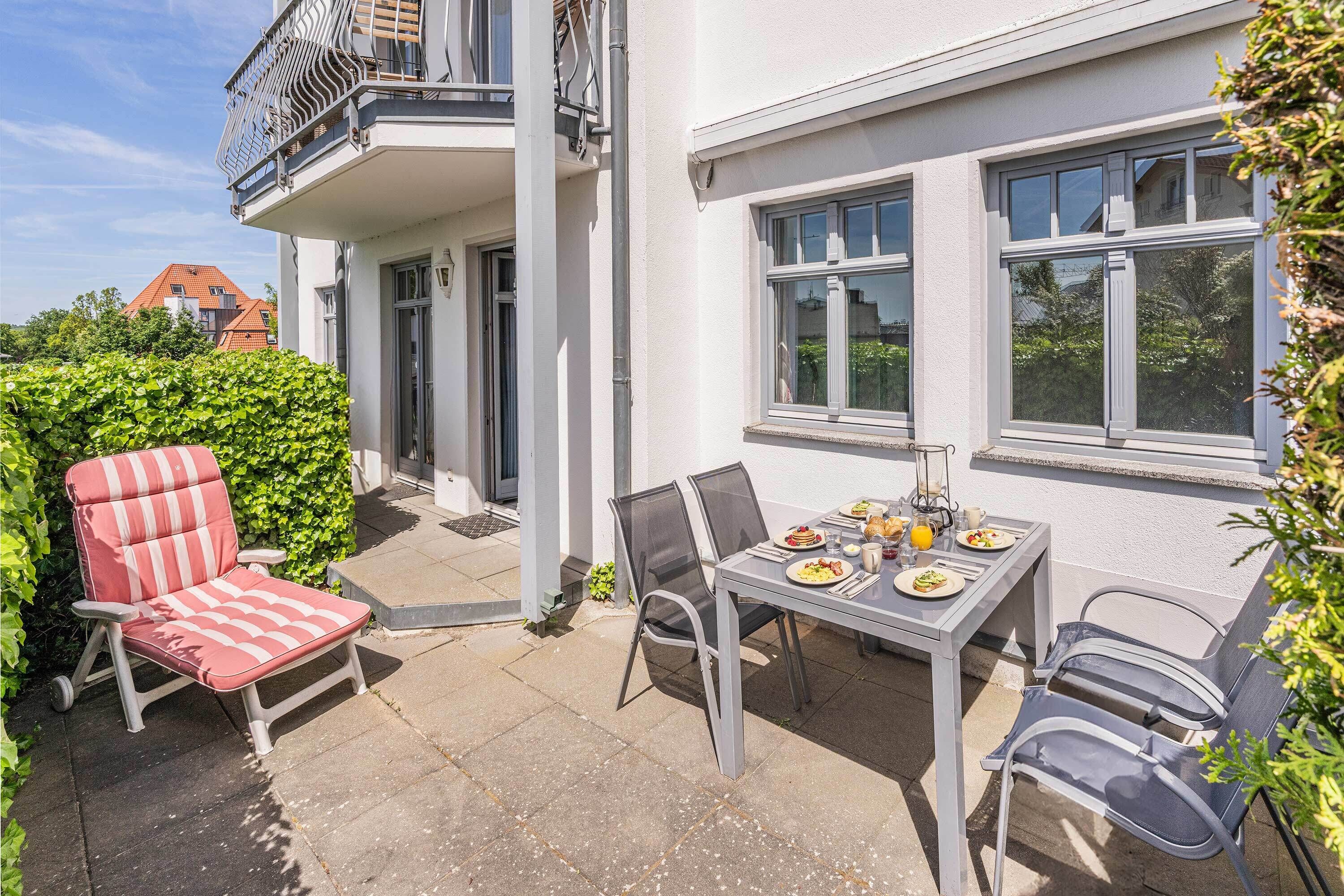 Un patio con una mesa lista para comer, sillas de exterior y una tumbona.