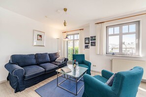 Un salon moderne avec un canapé, un fauteuil et une table, une fenêtre avec des rideaux et un radiateur.