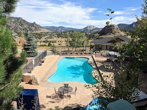 Une piscine avec vue sur les montagnes, un patio couvert et une terrasse délimitée par une clôture.