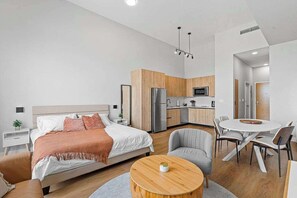 Ein modernes Schlafzimmer mit einem Bett, Nachttischen, einem runden Holztisch und einem grauen Sessel.