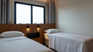 Ein Hotelzimmer mit zwei Einzelbetten, einem Holzkopfteil, einem Fenster mit Vorhängen und Wandleseleuchten.