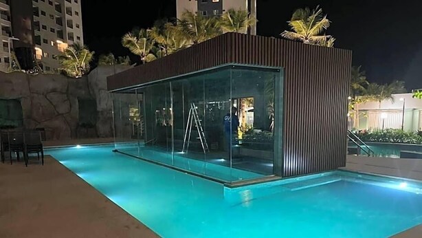 Ein Pool mit Glaswänden und moderner Architektur, umgeben von Palmen und Gebäuden.