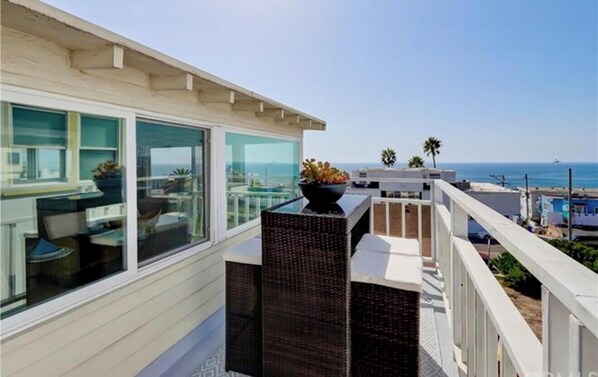 A balcony with a view of the ocean, a wicker planter, and a glass railing.