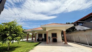 Una casa de dos pisos con un porche cubierto, un patio cercado y un cielo despejado.