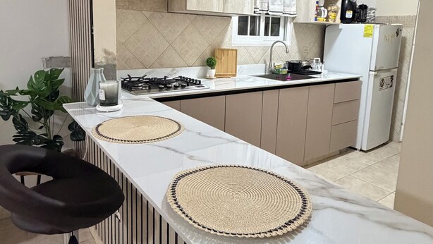 Una cocina moderna con una isla central, taburetes negros y vistas al comedor.