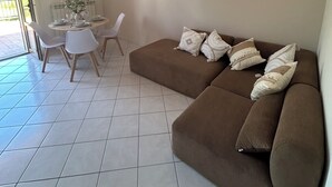 Ein modernes Wohnzimmer mit einem braunen Sofa, weißen Sesseln, einem Esstisch und einer Pendelleuchte.