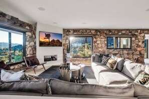 Ein modernes Wohnzimmer mit einer Wand aus Stein, einem großen Fenster mit Aussicht, einem Sofa, einem Couchtisch und einem Sessel.