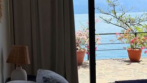 Un dormitorio con una cama, una lámpara y vistas a un lago y montañas a través de un ventanal.