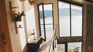 Una habitación amplia con piso de madera, pared de piedra y un gran ventanal con vista al agua.