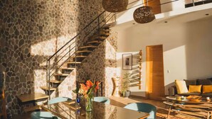 Un interior moderno con pared de piedra, escalera de madera, mesa de comedor de cristal y un sofá.