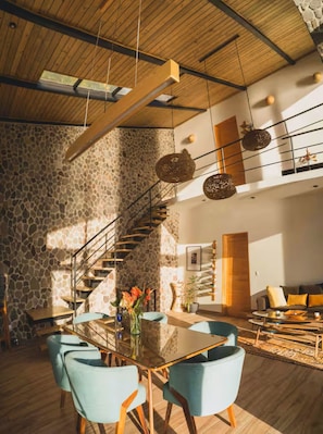 Un interior moderno con pared de piedra, escalera de madera, mesa de comedor de cristal y un sofá.
