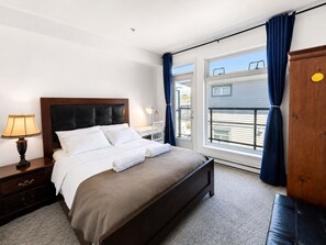 Ein Hotelzimmer mit Bett, Nachttisch, Lampe, Kleiderschrank und einem Fenster mit Vorhängen.