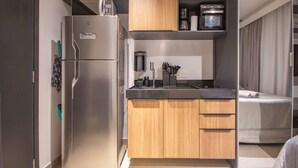 Eine kleine Küche mit Kühlschrank, Mikrowelle, Kaffeemaschine und kleinem Backofen. Ein Holzschrank beherbergt ein Spülbecken und eine Arbeitsplatte.
