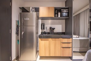 Eine kleine Küche mit Kühlschrank, Mikrowelle, Kaffeemaschine und kleinem Backofen. Ein Holzschrank beherbergt ein Spülbecken und eine Arbeitsplatte.