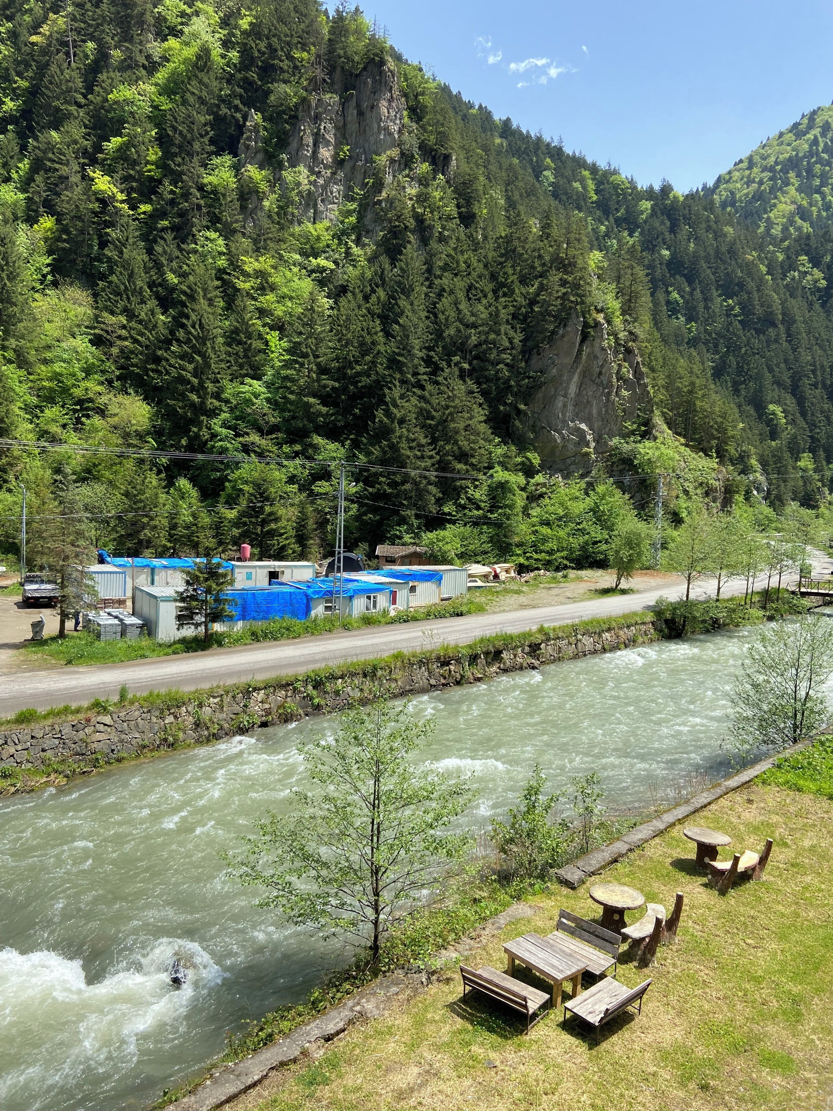 Un río con una zona de bancos de madera y un edificio con lonas azules al fondo.