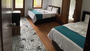A hotel room with two beds, a wardrobe, a desk, and a patterned rug. - soylu otel restoran (Caykara)