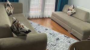 A living room with two sofas, a patterned rug, and a view through sheer curtains. - soylu otel restoran (Caykara)