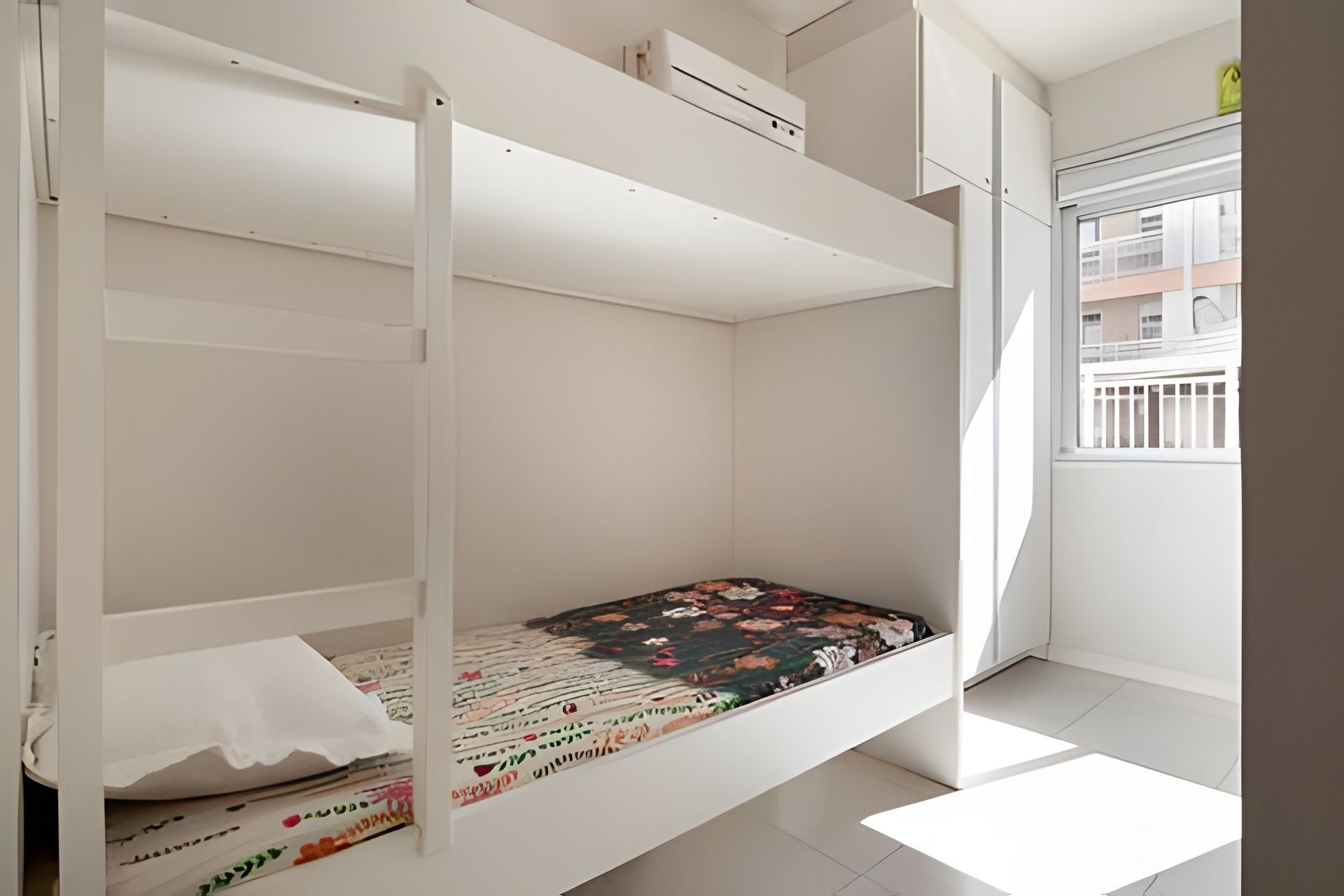 Ein Etagenbett mit Blumenmuster-Matratze, weiße Wände und ein Fenster mit Blick auf Gebäude.