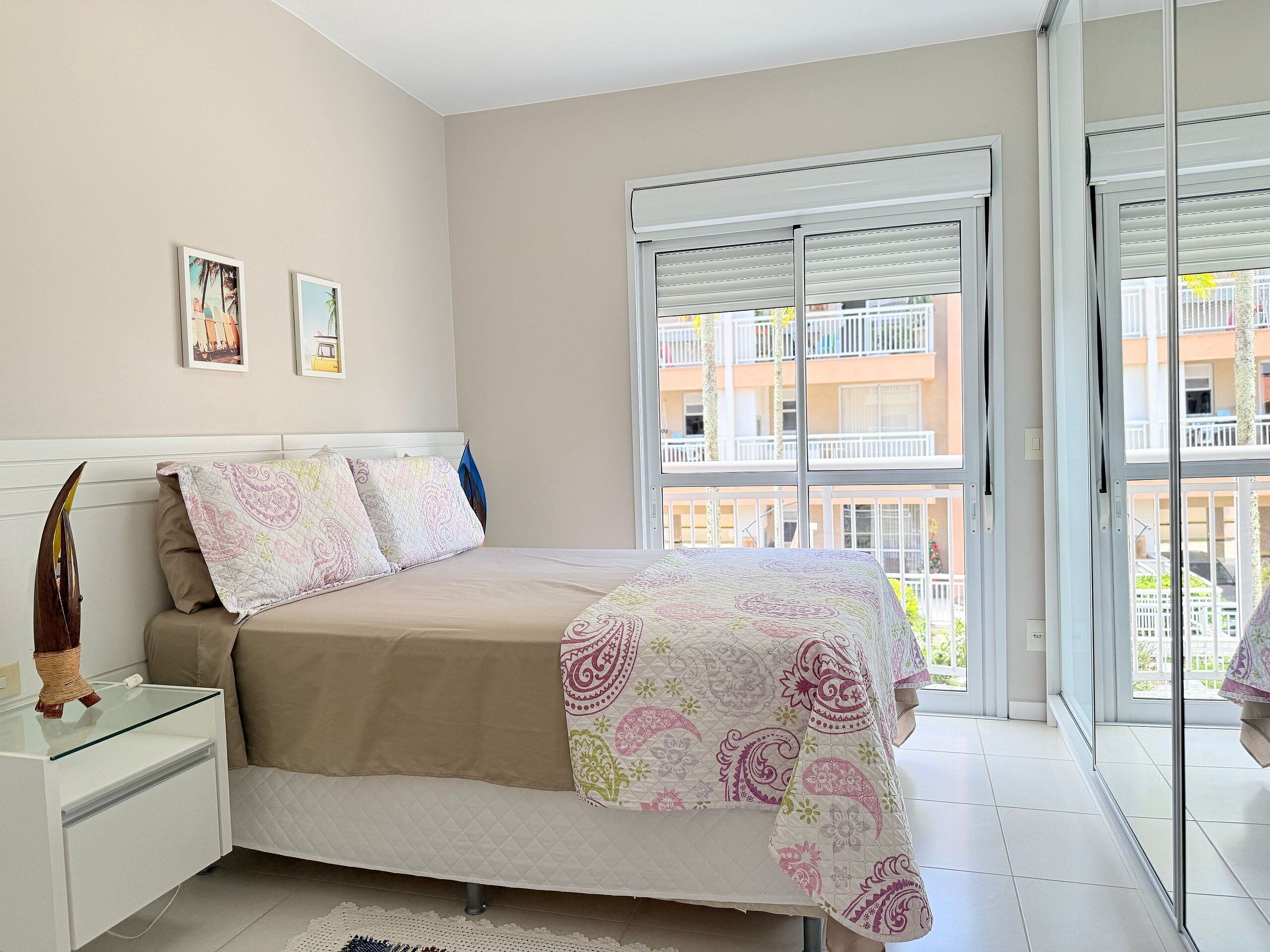 A bedroom with a bed, bedside tables, a window with a view of balconies, and a door.