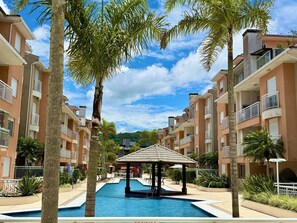 A residential building with balconies, a swimming pool, and a gazebo. - Residencial com piscina (Florianópolis)