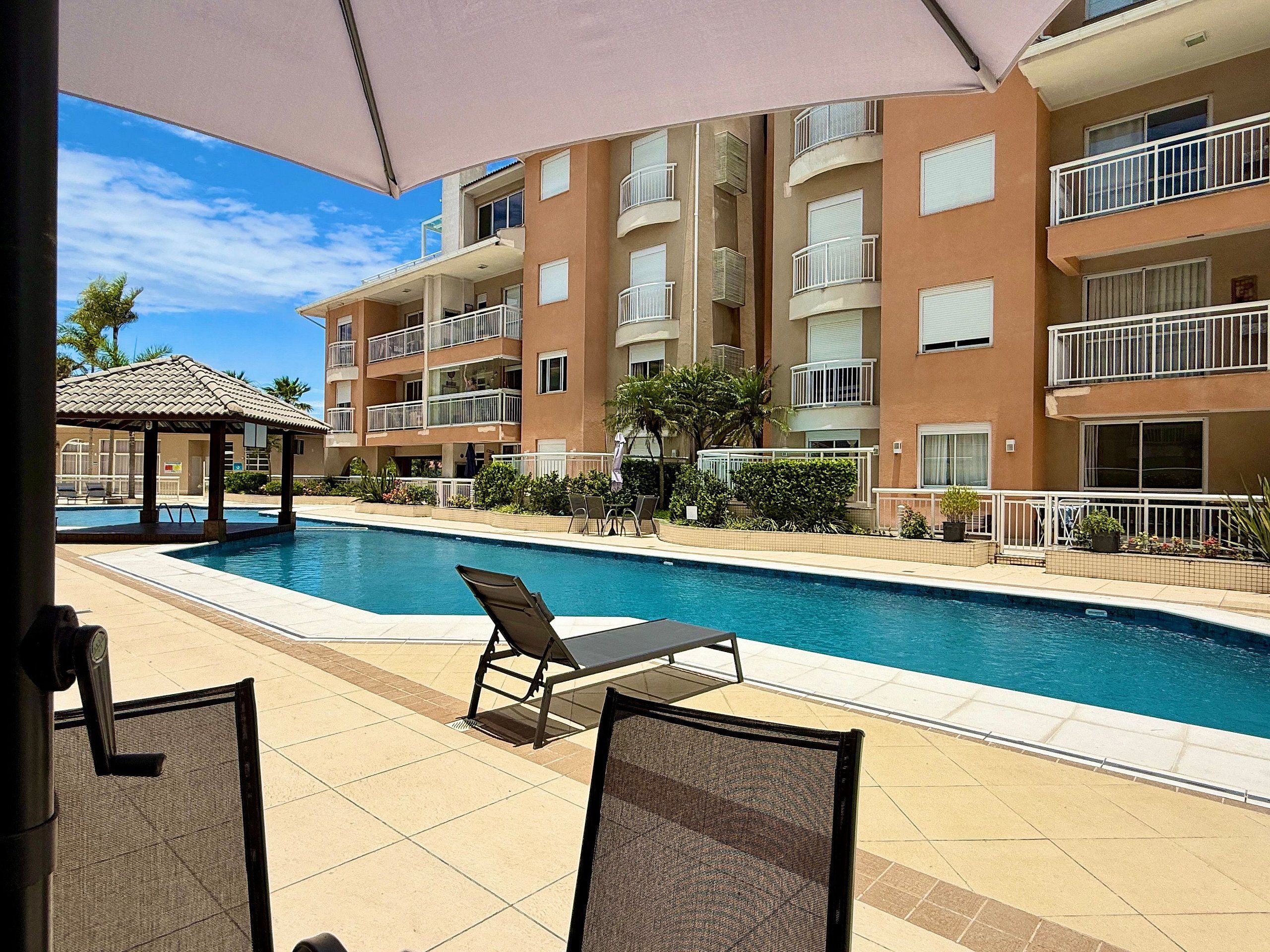 A swimming pool with lounge chairs, a covered area, and a multi-story building with balconies.