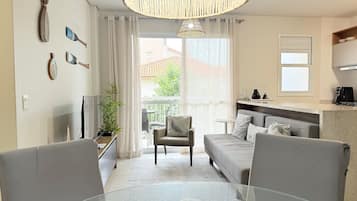 Una sala de estar moderna con sofá, sillas, mesa de comedor, televisor, planta y vistas al exterior.