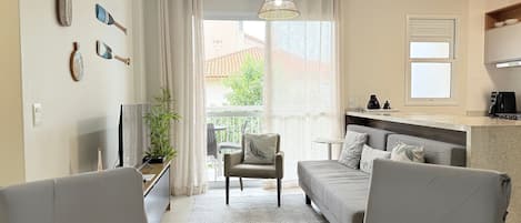 A modern living room with a sofa, chairs, a dining table, a TV, a plant, and a view of the outside.