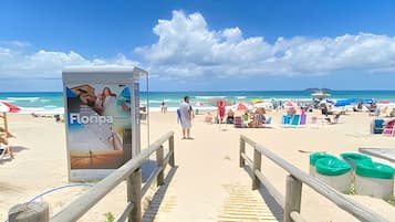 Een strand met een houten looppad dat naar de zee leidt, een bord en strandparasols.