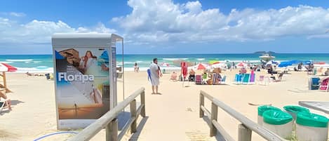 A beach with a wooden walkway leading to the sea, a signboard, and beach umbrellas.