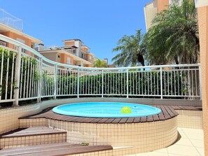 Una piscina con borde de baldosas, rodeada por un cerco blanco y follaje.