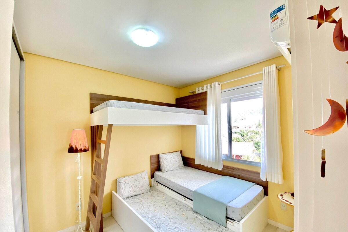 A bunk bed room with a window, a bedside lamp, and a wall decoration.