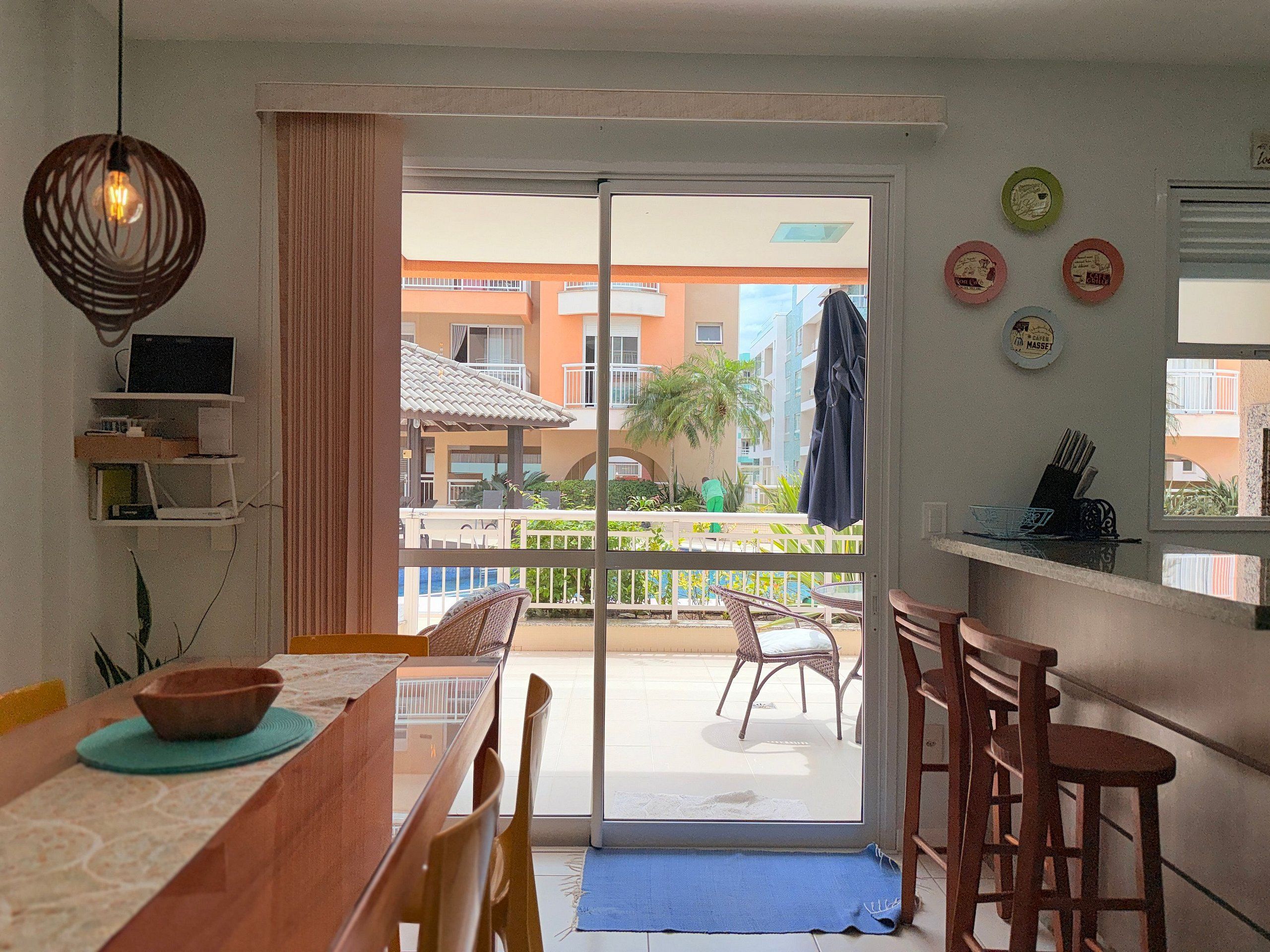 A dining area with a table, chairs, a laptop, and a view of a balcony with outdoor furniture.