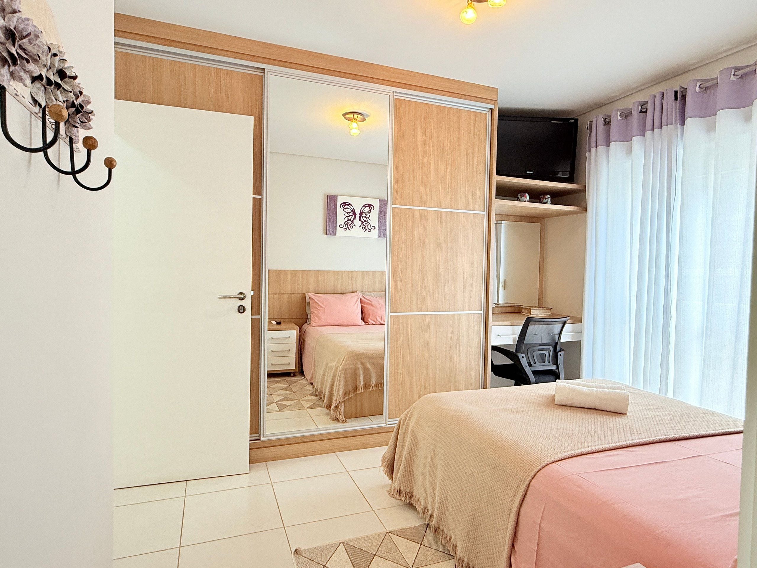 A bedroom with a bed, a desk, a wardrobe, and a mirror.