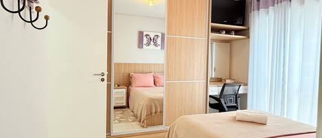 A bedroom with a bed, a desk, a wardrobe, and a mirror.