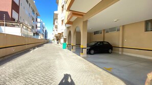 Un estacionamiento con un coche dentro, cielo despejado y edificios al fondo.