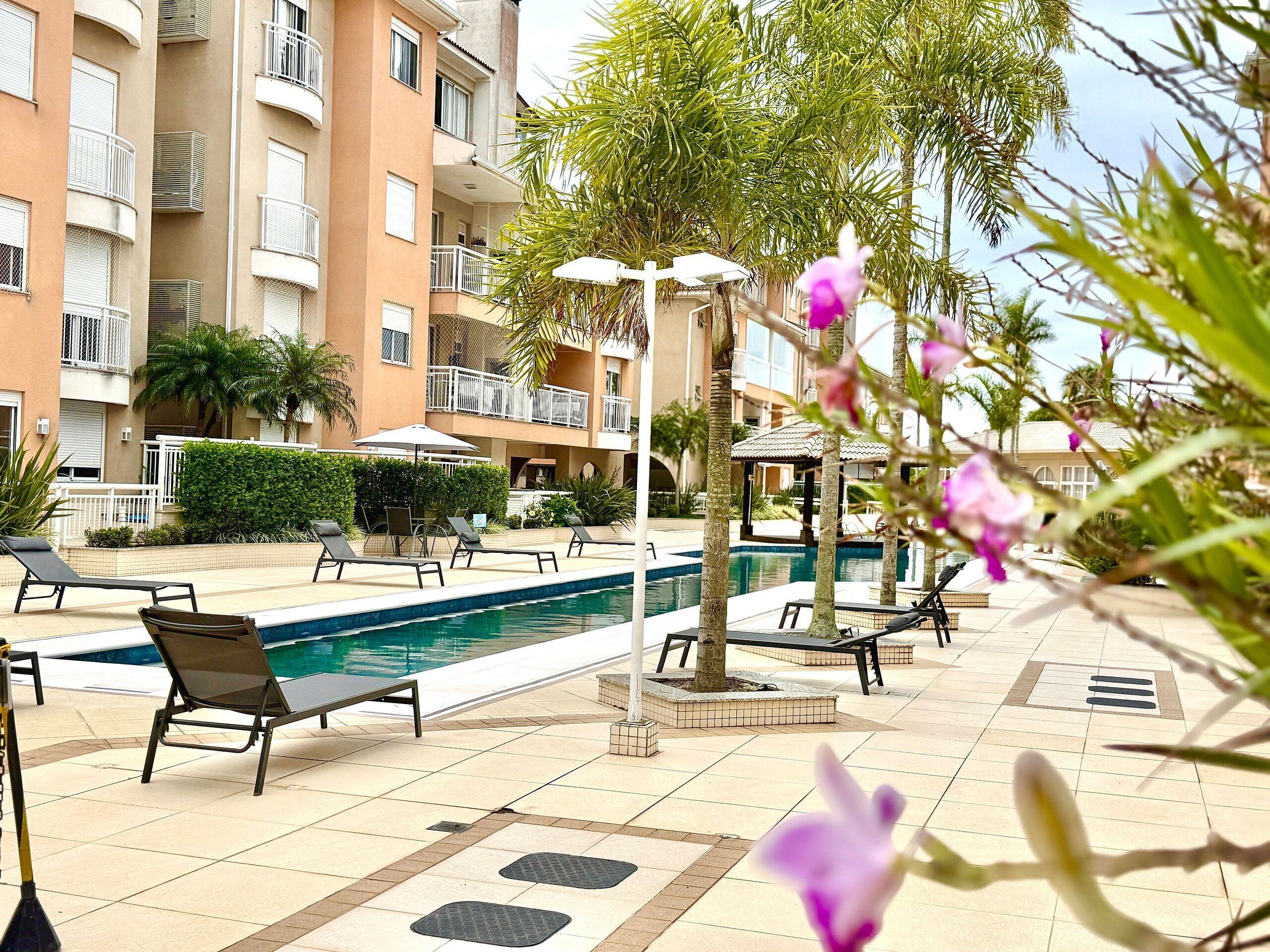 Zona de piscina con sillones de descanso, una piscina y un edificio con balcones.