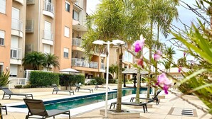A poolside area with lounge chairs, a pool, and a building with balconies.