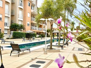 A poolside area with lounge chairs, a pool, and a building with balconies. - Residencial com piscina (Florianópolis)