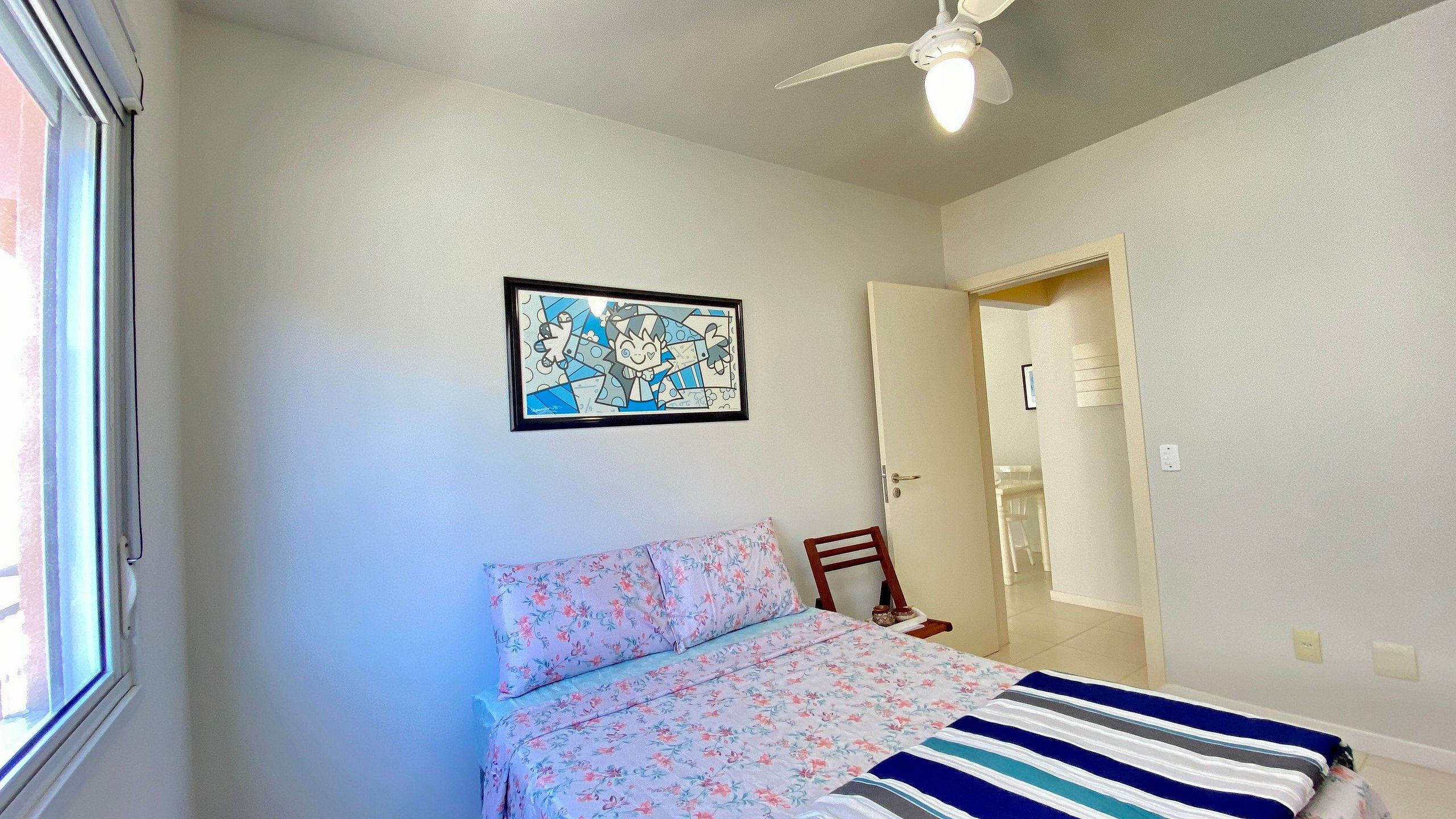 Een slaapkamer met een bed, een plafondventilator, een ingelijst schilderij aan de muur en een deur naar een andere kamer.