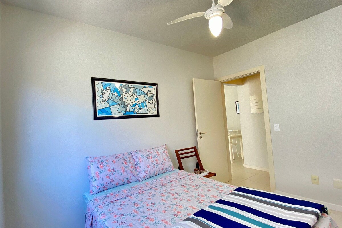 A bedroom with a bed, a ceiling fan, a framed picture on the wall, and a door leading to another room.