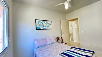 Een slaapkamer met een bed, een plafondventilator, een ingelijst schilderij aan de muur en een deur naar een andere kamer.