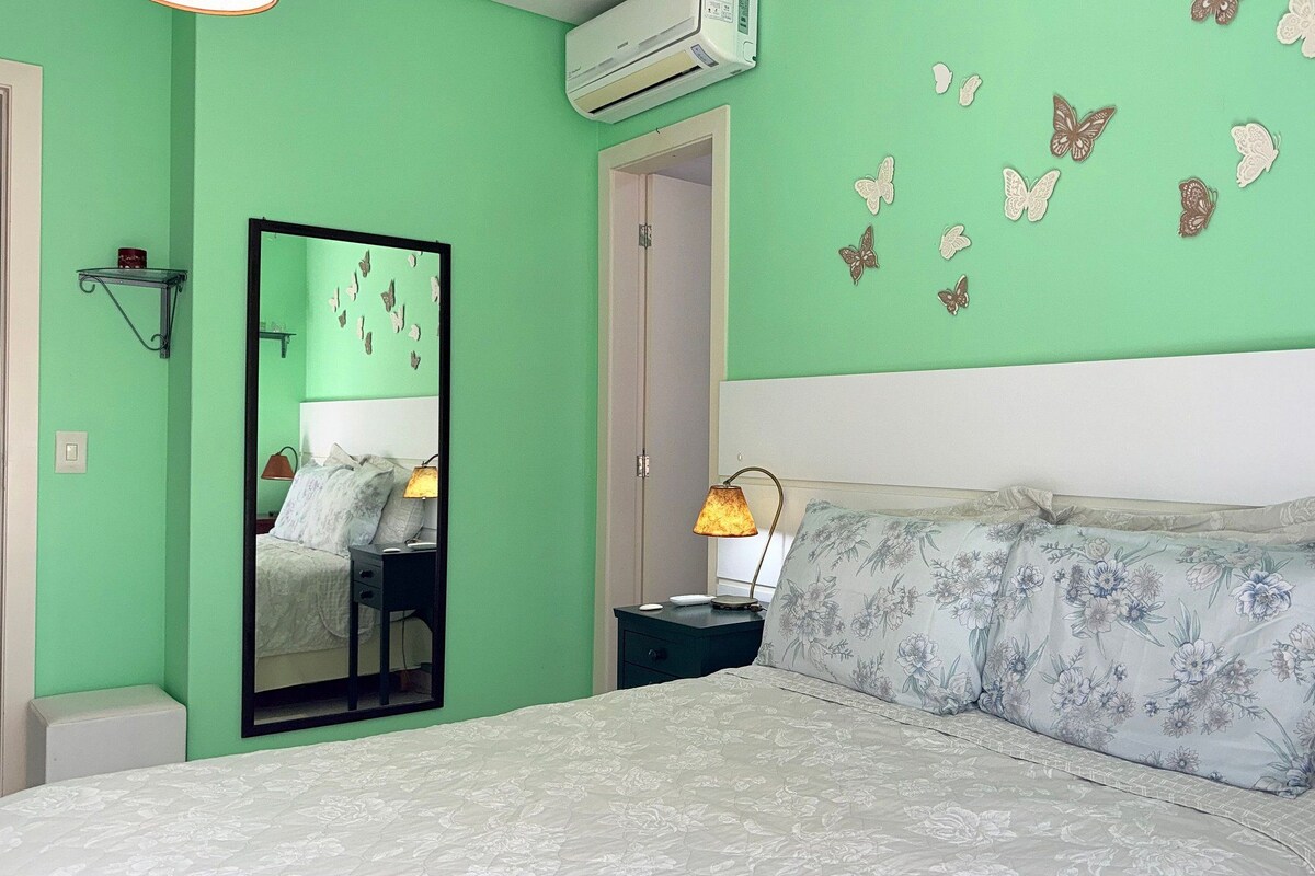 A bedroom with a bed, a nightstand, a lamp, a mirror, and butterfly wall decorations.