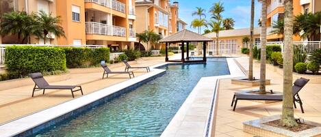 A swimming pool with lounge chairs, a gazebo, and palm trees.