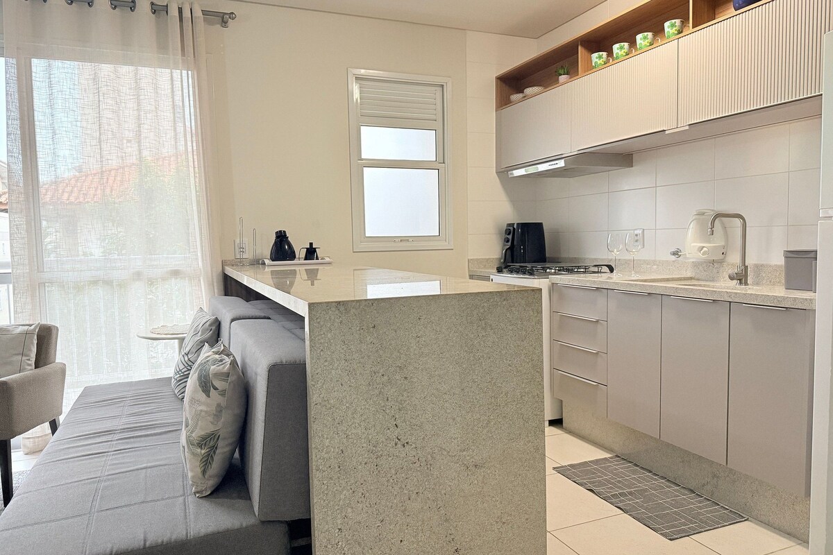 A modern kitchen with a central island, a dining area with a sofa, and a window with curtains.